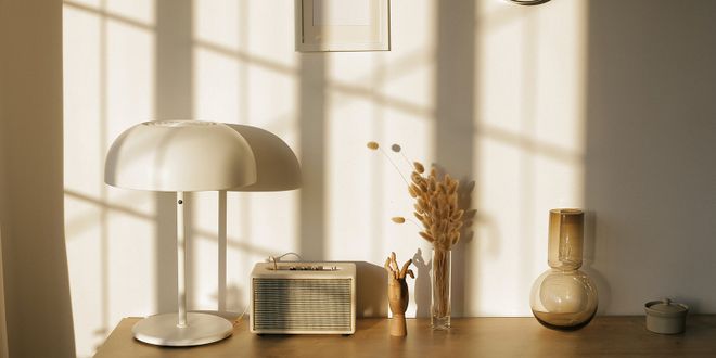 Sideboard mit einer weißen Stehlampe, einem Radio und zwei Glasvasen, eine davon mit Trockenblumen.