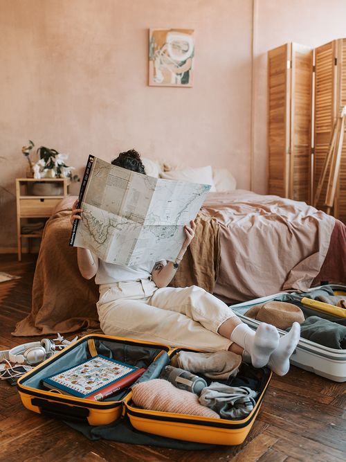 Frau sitzt vor dem Bett mit offenen Koffern liest eine Landkarte.