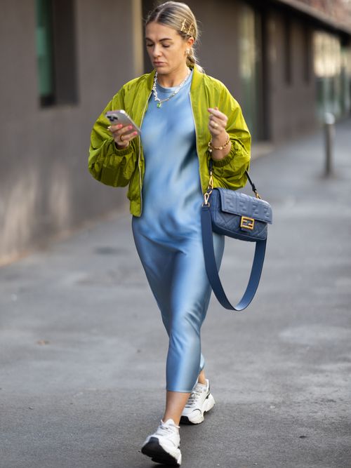 Street Style Look von der Milan Fashion Week, wo ein Gast ein Satinkleid mit Bomberjacke und Sneaker trägt.