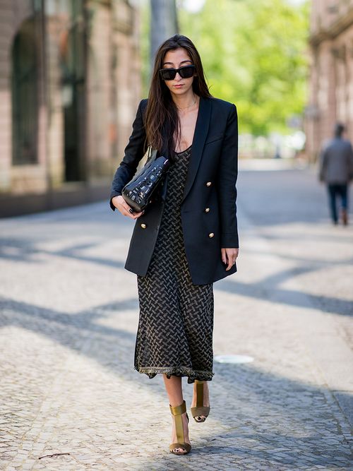 Frau trägt olivfarbenes langes Kleid, mit goldenen Pumps und schwarzen Boyfriend Blazer