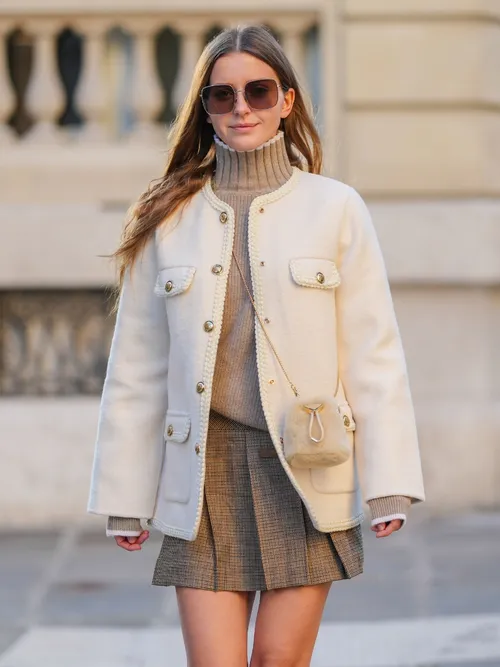 Diane Batoukina wears brown Dior sunglasses, a brown Sandro turtleneck pullover, a white wool Sandro jacket, a light brown fluffy faux fur Prada bag, a brown Sandro mini skirt, during a street style fashion photo session, on January 13, 2025 in Paris, France.