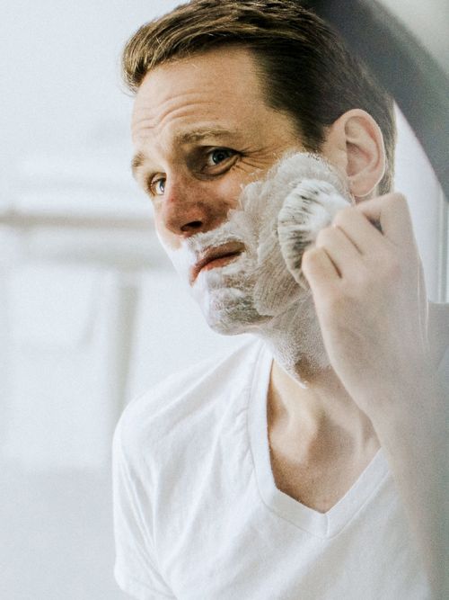 Mann steht vor dem Spiegel im Badezimmer und rasiert sich