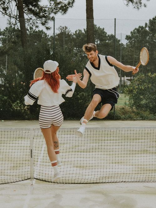 Paar am Tenniscourt, das in die Luft springt und sich abklatscht.