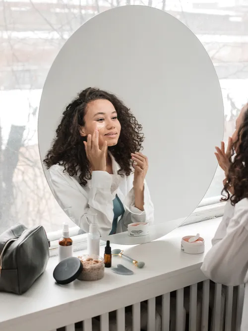 Junge Frau mit lockigem Haar klebt sich eine Augenpad aufs Gesicht.
