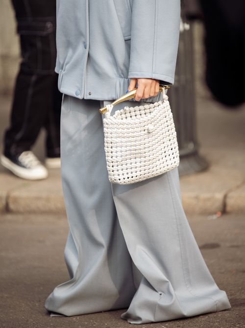 Street Style Look von der Milan Fashion Week, wo ein Gast einen hellblauen Hosenanzug mit weißer Häkel-Tasche trägt.