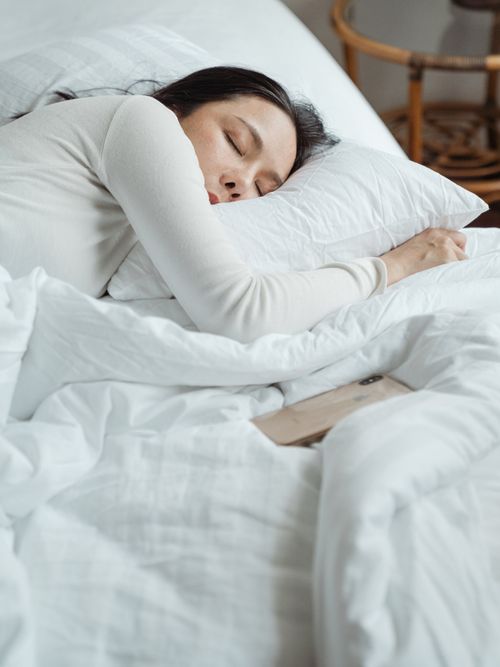 Eine Frau, die in weißer Bettwäsche gehüllt, schläft.