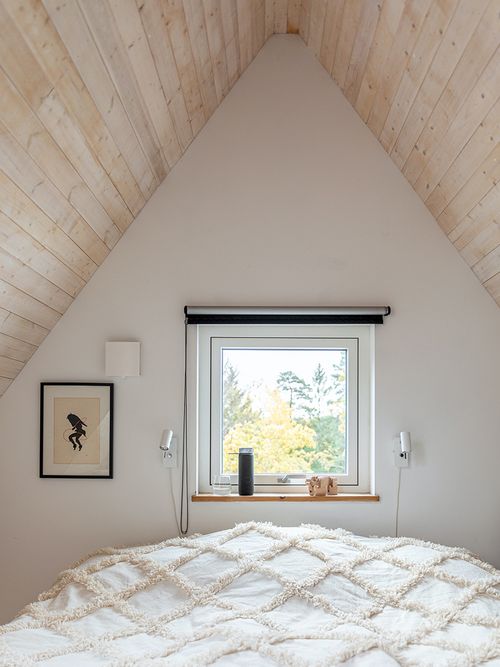Schlafzimmer unter einer mit hellem Holz verkleideten Dachschräge und einem Fenster.