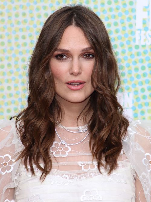 Keira Knightley mit gewellten Haaren und einem weißen Spitzenoberteil.