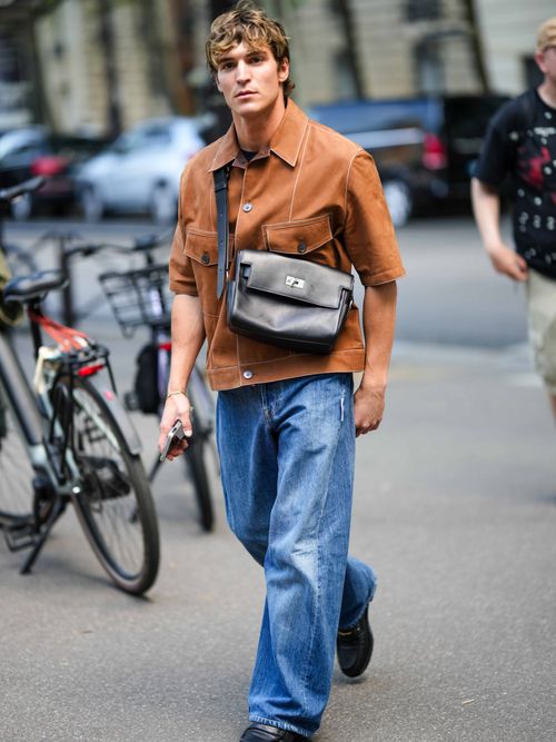 Street Style Look von der Paris Fashion Week, wo ein Gast ein braunes Kurzarmhemd mit Crossbody-Bag, Baggy-Jeans und Loafers trägt.