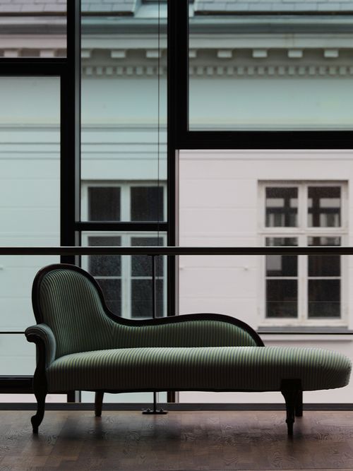 Ein grüner Chaiselounge vor einer Fensterfront.