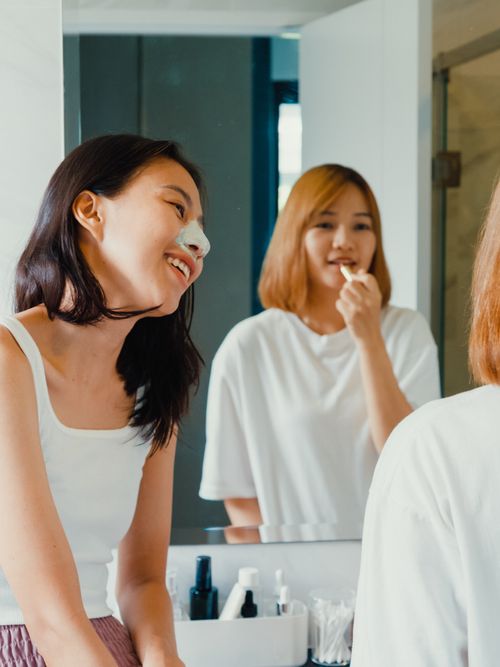 Zwei Mädels im Badezimmer vor dem Spiegel, wo sich die eine Zähne putzt.