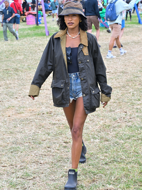 Saffron Hocking trägt eine Barbour Jacke mit schwarzem Top und Denim-Hotpants sowie Hunter Boots am Glastonbury Festival.