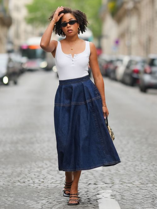 Ellie Delphine trägt ein weißes Tanktop, schwarze Sonnenbrille, Sandalen und einen Midirock aus Jeans in Paris.
