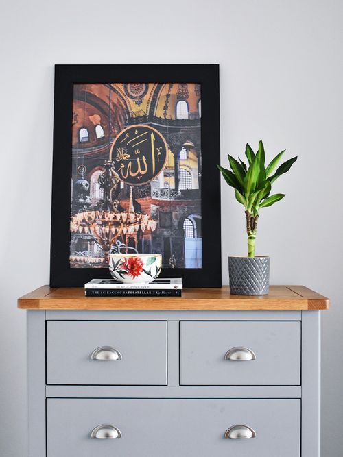 Bild ener grau gestrichenen Kommode, auf der einen Pflanze und ein Bild mit schwarzen Rahmen steht.