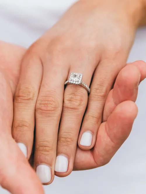 Mann hält Frauenhand mit Verlobungsring und weißem Nagellack