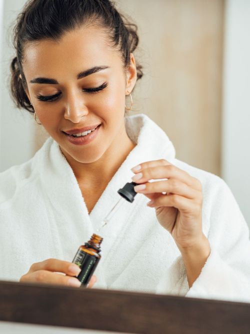 Frau im Badezimmer trägt einen Morgenmantel und ist dabei sich Rizinusöl aufzutragen