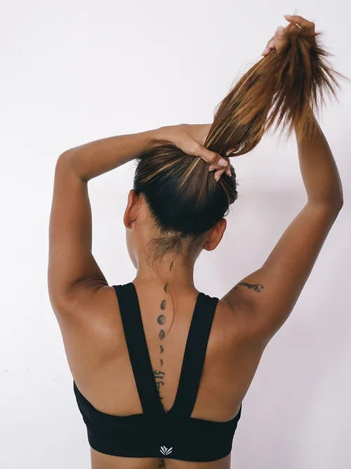 Frau die sich ihre braunen Haare gerade zum Pferdeschwanz zusammenbindet.