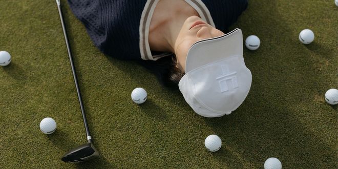 Frau mit weißem Cap liegt auf der Wiese und neben ihr liegen 3 Golfbälle und ein Schläger.