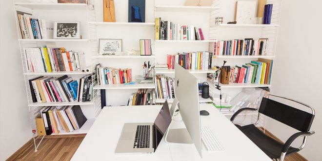Weißer Schreibtisch mit zwei PCs vor einer weißen Bücherregalwand.