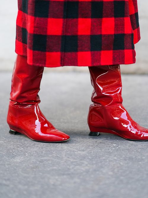 Close up von roten Lackstiefeln zu einem rot/schwarz karierten Mantel.