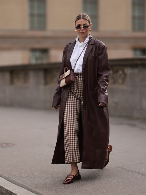 Aline Kaplan trägt einen Ledermantel, weiße Bluse und karierte Hose in Berlin.
