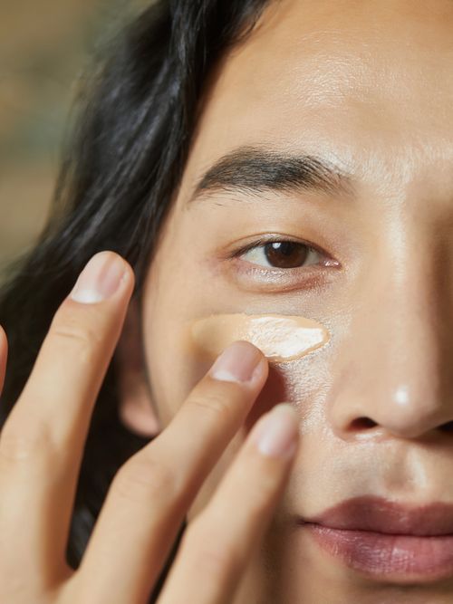 Ein asiatischer Mann trägt sich gerade eine Gesichtscreme auf.