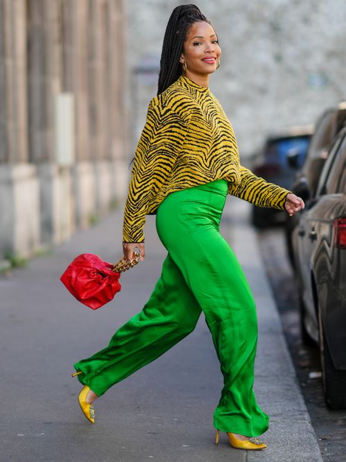 Ellie Delphine trägt ein Zebra-Oberteil in Gelb, eine grüne Hose, gelbe Pumps und rote Tasche in Paris.