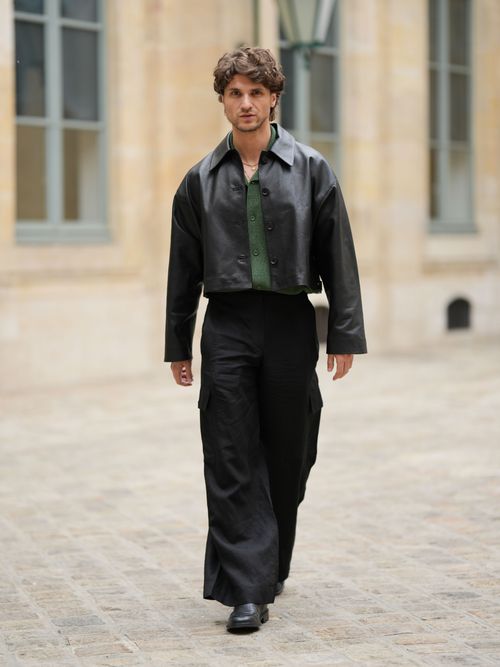 Street Style Look von der Paris Fashion Week, wo ein Gast eine schwarze Lederjacke mit grünem T-Shirt und schwarze Hose trägt.