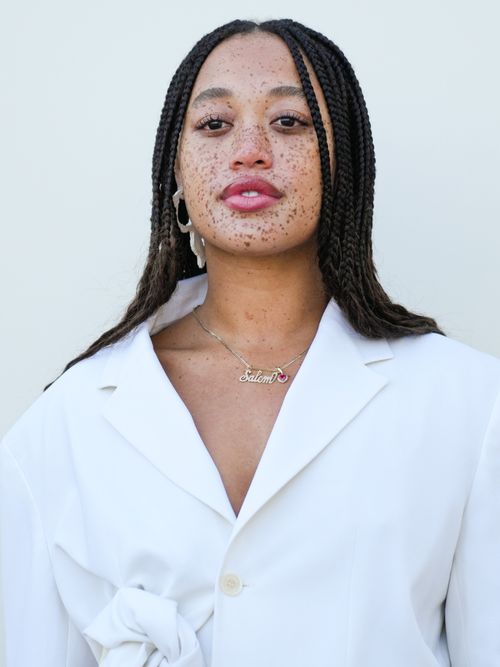 Ein Model mit Sommersprossen trägt einen weißen Blazer und Statement-Schmuck auf der Jacquemus Show in Frankreich.