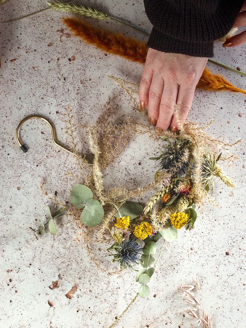 Ein Tisch auf dem ein Kranz aus Trockenblumen liegt und eine Hand greift danach.