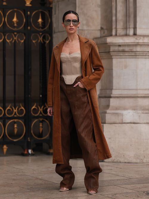 Alexandra Guerain trägt eine beige Korsage, braunen Wildledermantel, braune Hose, High Heels und Sonnenbrille auf der Paris Fashion Week.