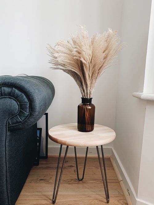 Pampasgras in einer braunen Glasvase auf einem runden Beistellstisch mit schwarzen Beinen.
