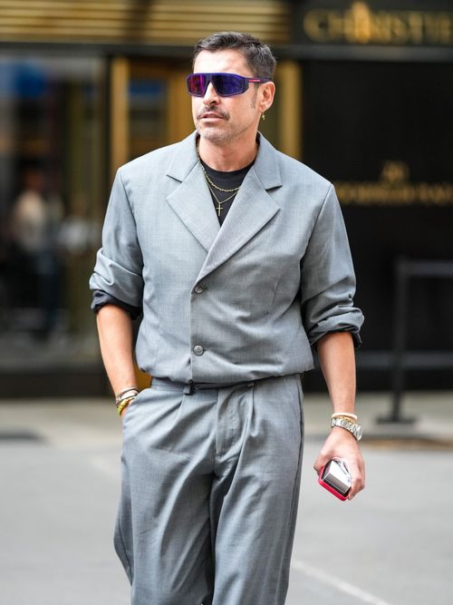 Alex Badia trägt einen grauen Anzug mit schwarzem T-Shirt und goldene Ketten. Dazu eine sportliche Sonnenbrille auf der New York Fashion Week.