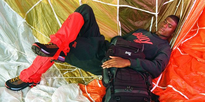 Mann liegt in einem Paragleitingschirm, mit einem Wanderrucksack