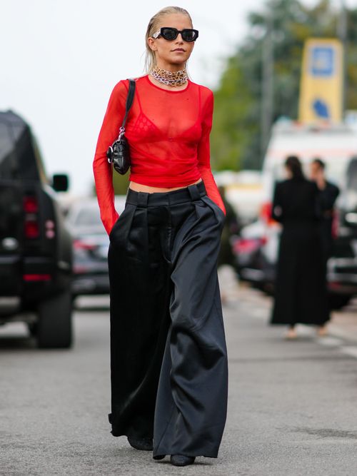 Caroline Daur trägt ein Sheer-Oberteil in Rot, breiter schwarzen Hose und Statement-Kette auf der Paris Fashion Week.