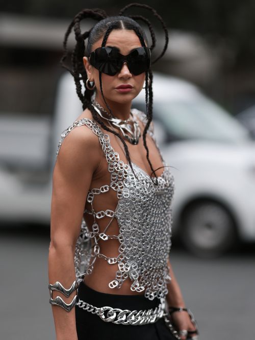 A Fashion Week guest is wearing large black sunglasses from Balenciaga, two large necklaces in silver, a shiny silber top consisting of tear tabs of cans and carabiner with cut-out of the back, a large silver bracelet, many silver rings, wide black pants with two big white trouser pockets and a black leather handbag from Coperni outside Amiri Show during the Menswear Spring/Summer 2024 as part of Paris Fashion Week on June 22, 2023 in Paris, France.