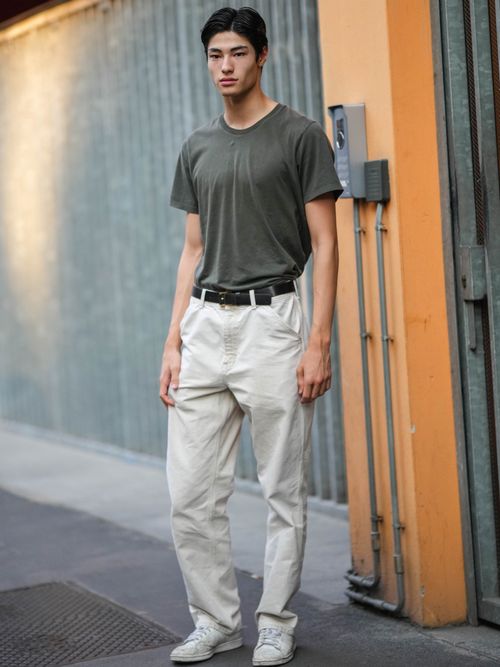 Street Style Look von der Milan Fashion Week, wo ein Gast ein khakifarbenes T-Shirt mit weißer Chino und Gürtel, sowie weiße Sneakers trägt.