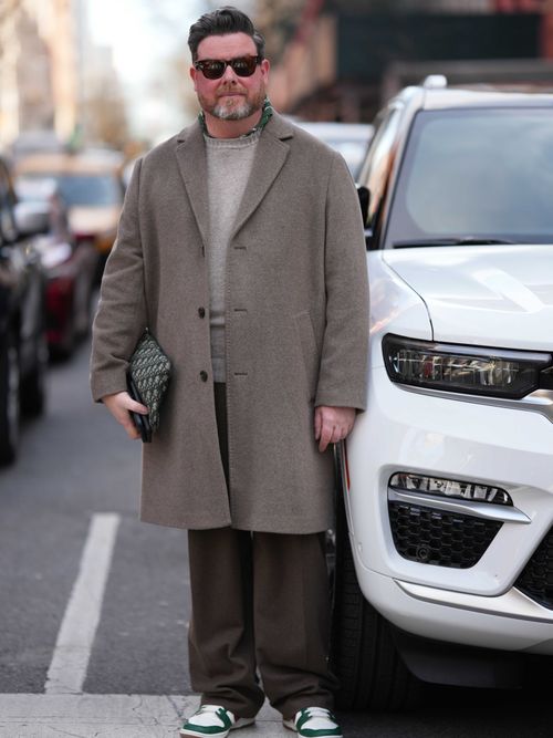 Street Style Look von der New York Fashion Week, wo ein Gast einen grauen Mantel mit hellgrauen Shirt und brauner Hose trägt.