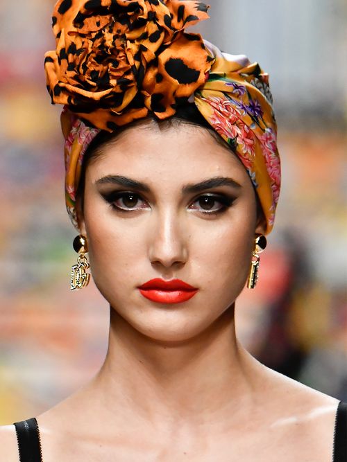 Close up vom Runway von einer Frau mit rotem Lippenstift und einem orangefarbenen Kopftuch.