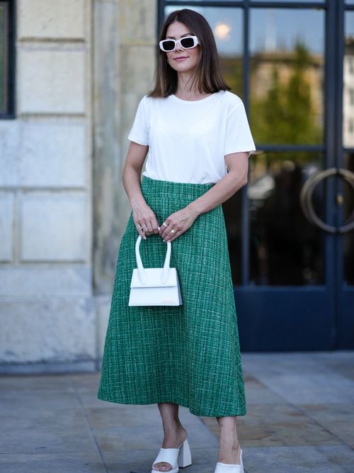 Ein Gast auf der Copenhagen Fashion Week trägt ein weißes T-Shirt mit einem grünen Midirock, mit weißer Sonnenbrille und weißer Handtasche.