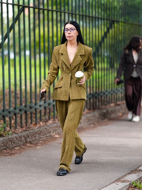 A guest wears dark velvet green oversized blazer jacket, dark green loose pants, shiny black loafer moccasin leather shoes , outside Gucci, during the Milan Fashion Week Spring/Summer 2024-2025 on September 20, 2024 in Milan, Italy.