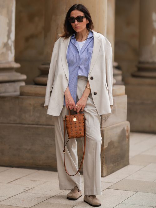 Elise Seitz trägt einen weißen Blazer, blaue Bluse und beige Hose mit einer Mcm Tasche in München.