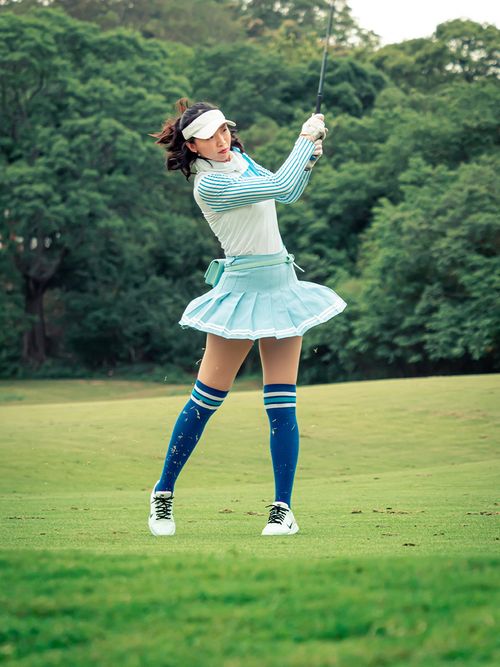 Frau mit kurzem Faltenrock und Overknee-Socken am Golfen.