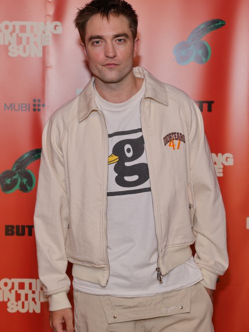 Robert Pattinson auf dem Red Carpet und trägt eine beige Hemdjacke mit weißem T-Shirt und beige Hose.