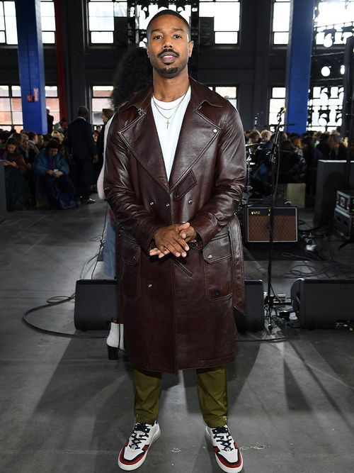Michael B. Jordan in einem braunen Ledermantel und Sneakers.