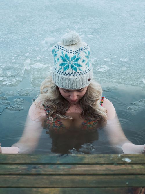 Eine Frau, die mit Strickmütze und Badeanzug ins Eiswasser baden geht.