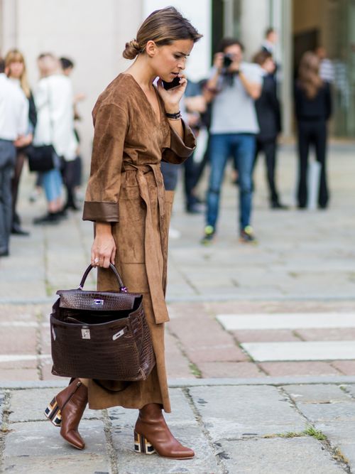 Miroslava Duma trägt einen Wildledermantel in Braun mit braunen Stiefel und hält eine Hermes Birkin Bag auf der Milano Fashion Week.