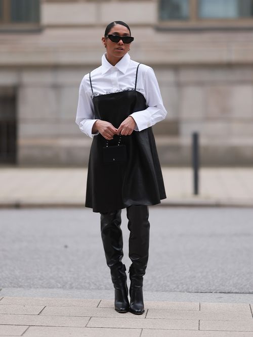 Cherifa Akili trägt eine schwarzes Trägerkleid mit weißer Bluse darunter und schwarze Overknees in Hamburg.