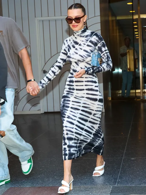 Millie Bobby Brown is seen leaving 'Today' Show on September 14, 2023 in New York City wearing a tie-dye blue and white maxi dress, tortoiseshell sunglasses, a light blue clutch bag, and white heeled sandals.