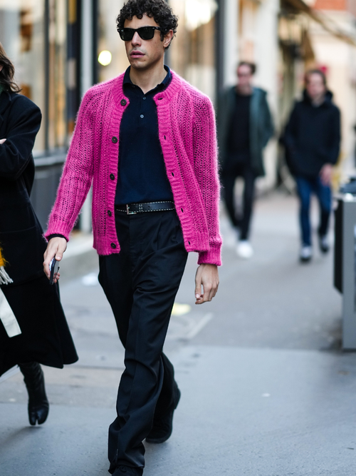 Street Style Look von der Paris Fashion Week, wo ein Mann einen pinken Cardigan mit schwarzem Hemd und schwarzer Hose trägt.
